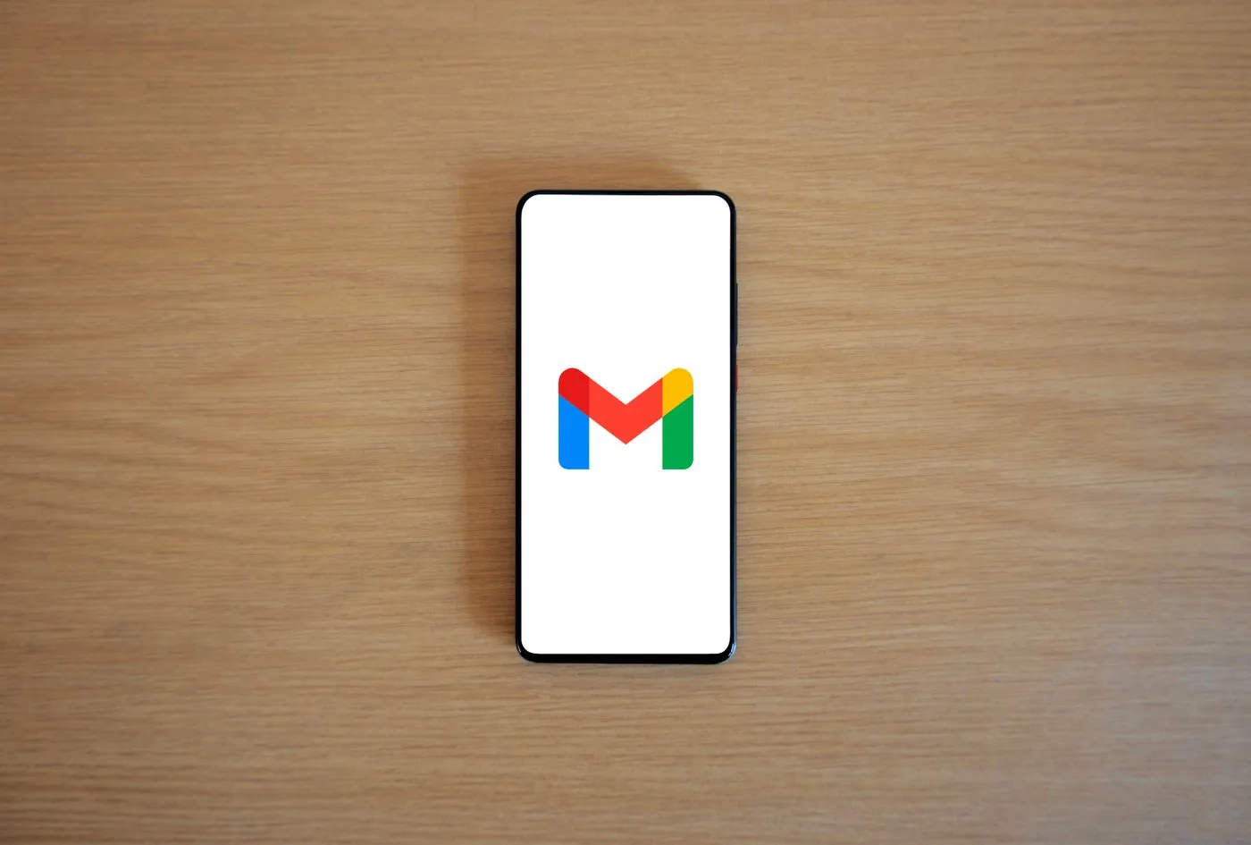 Teléfono con el logo de Gmail en pantalla sobre un escritorio de madera: el correo sigue siendo la puerta de entrada principal del phishing en las empresas