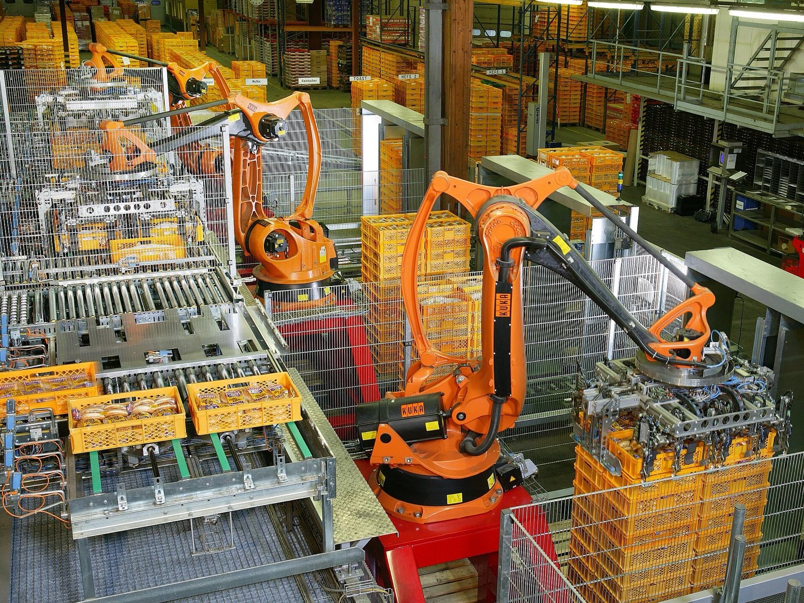 Brazos robóticos paletizando cajas dentro de jaulas de seguridad en una planta de producción