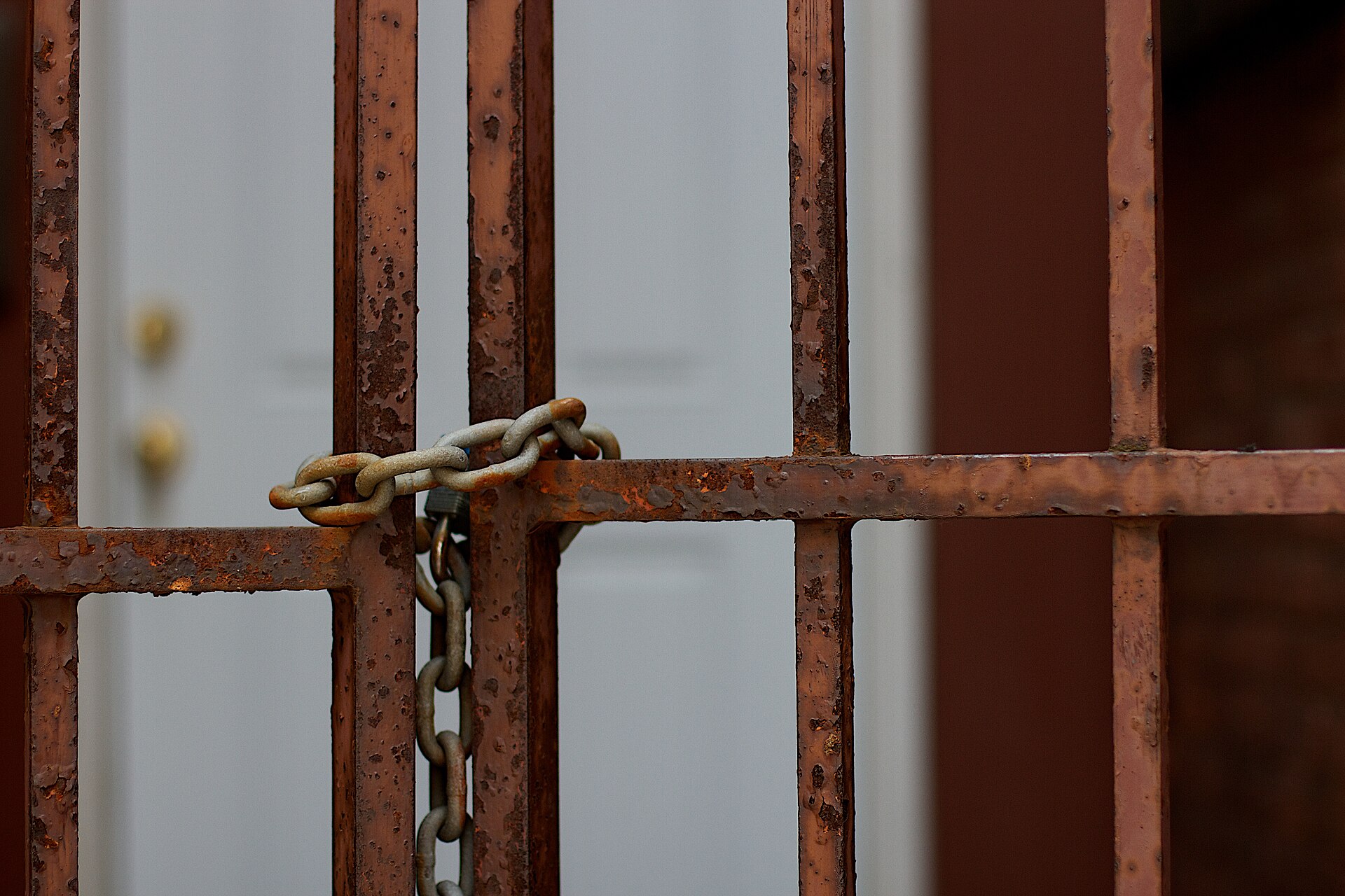 Portón de rejas oxidado cerrado con una cadena y un candado, con una puerta abierta detrás