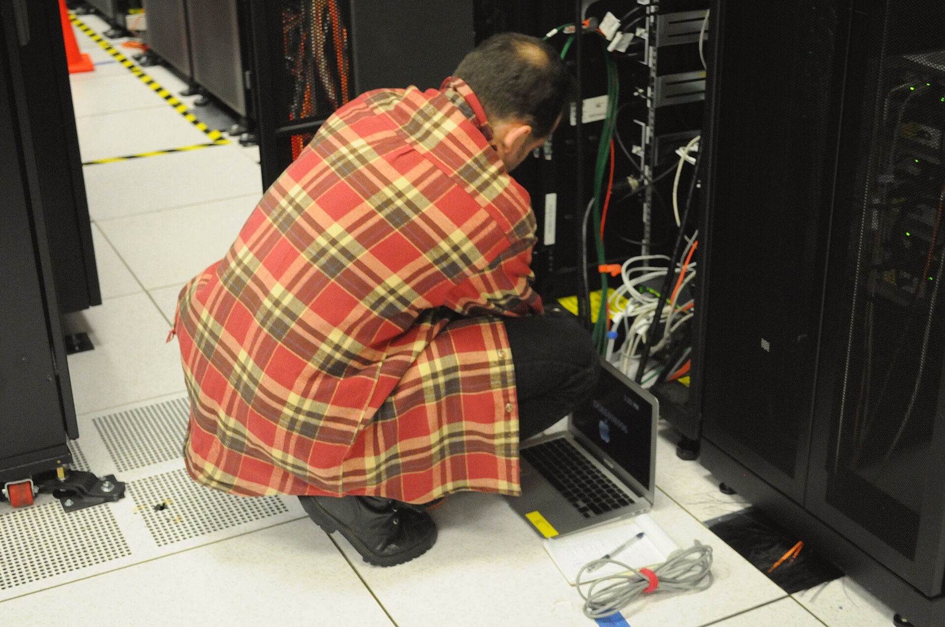 Técnico agachado con una notebook trabajando sobre el cableado de un rack de servidores