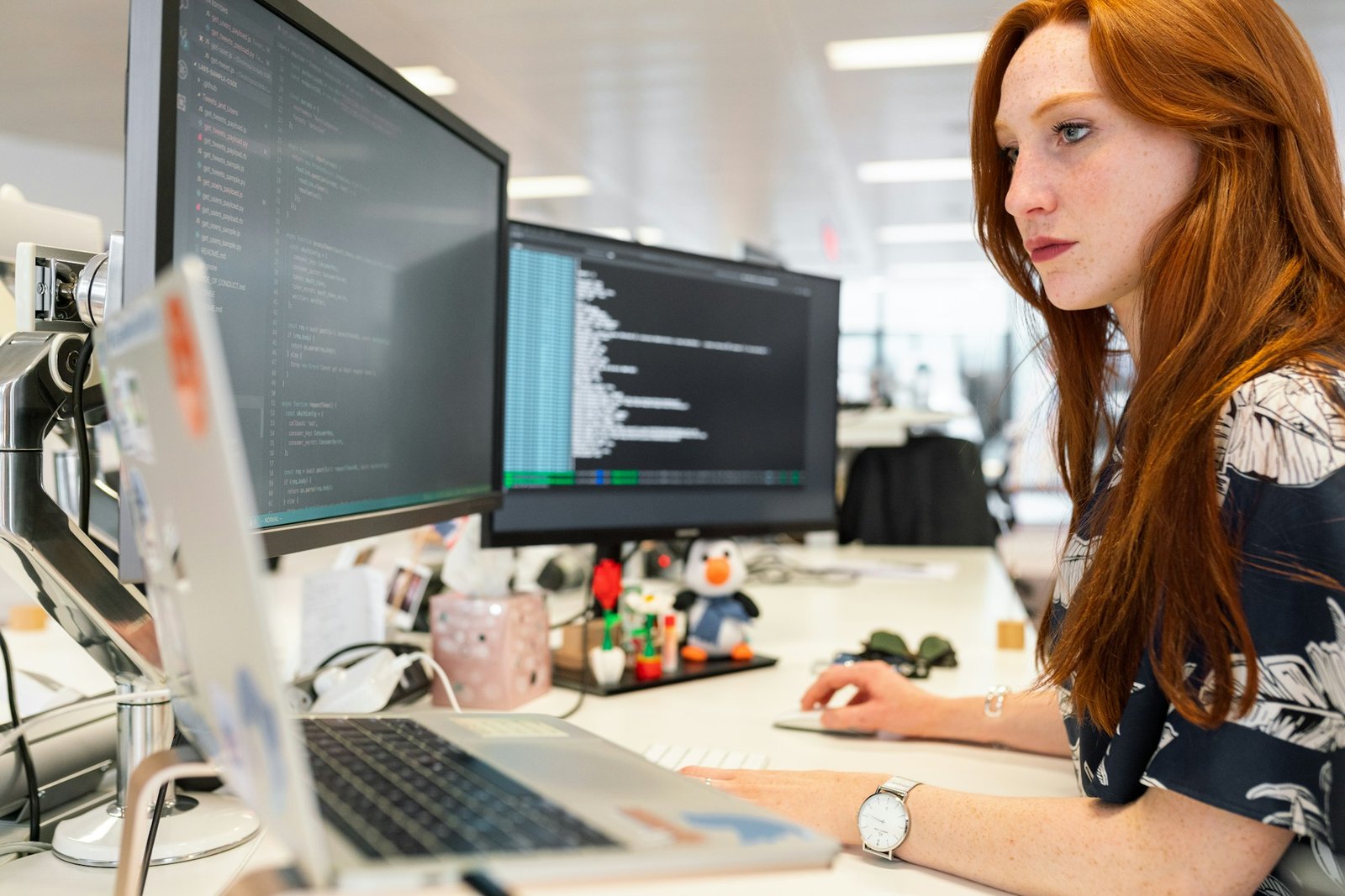 Persona del área de sistemas trabajando con dos monitores y una notebook